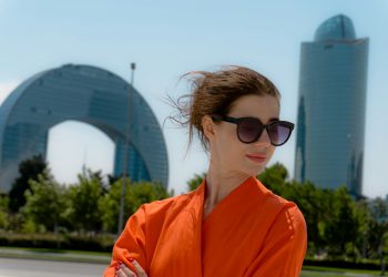 Woman in orange dress with sunglasses and buildings