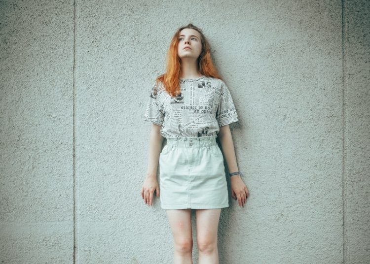 Young woman with red hair leaning against wall