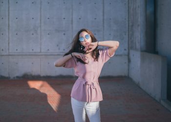 woman in pink sleeveless shirt and white pants standing on brown wooden floor