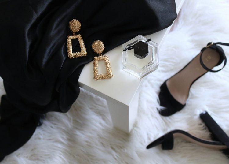 pair of gold-colored earrings on table and black ankle-strap pumps on area rug