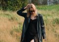 Woman in black coat walking through dry grass field.