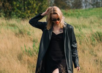 Woman in black coat walking through dry grass field.