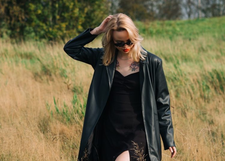 Woman in black coat walking through dry grass field.
