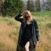 Woman in black coat walking through dry grass field.